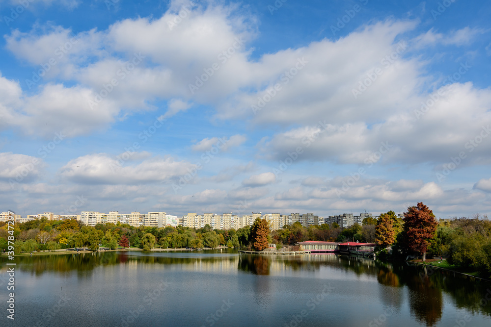 Landscape with many large green and yellow old trees near the lake in a sunny autumn day in Tineretului Park in Bucharest, Romania . Landscape with many large green and yellow old trees near the lake in a sunny autumn day in Tineretului Park in Bucharest, Romania .