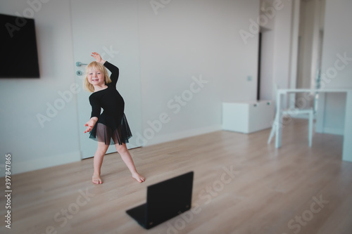 Ballet lesson online. Little girl dancing while looking at computer at home.