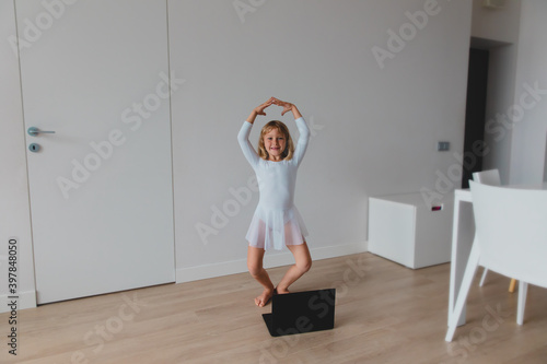 Ballet lesson online. Little girl dancing while looking at computer at home.