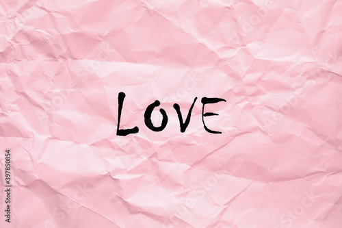 Word Love written on crumpled pink paper, top view