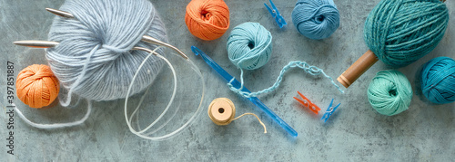Various wool yarn and knitting needles, creative knitting hobby. Panoramic background in pastel colors on textured grey green background.