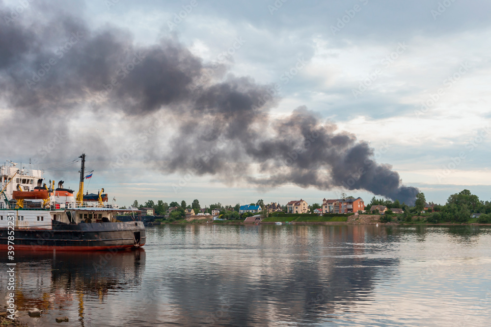 view across the river to a dangerous cloud of black smoke from a burning house. Fire and disaster concept