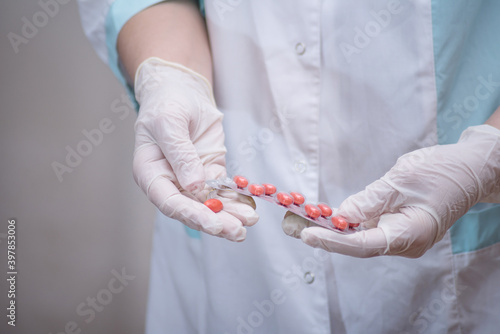 medical practitioner wearing surgical latex gloves holding medicine bottle,taking out several white pills,COVID-19 corona virus disease epidemic,Coronavirus global pandemic