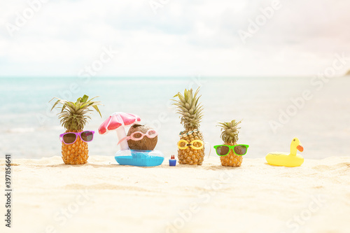 Family of funny attractive pineapples in stylish sunglasses on the sand against turquoise sea. Wearing christmas hats. Christmas and new year vacation concept on tropical beach. Family holiday. Bright