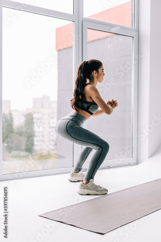 Full length view of an active woman in her working out and doing some squats at home © dianagrytsku