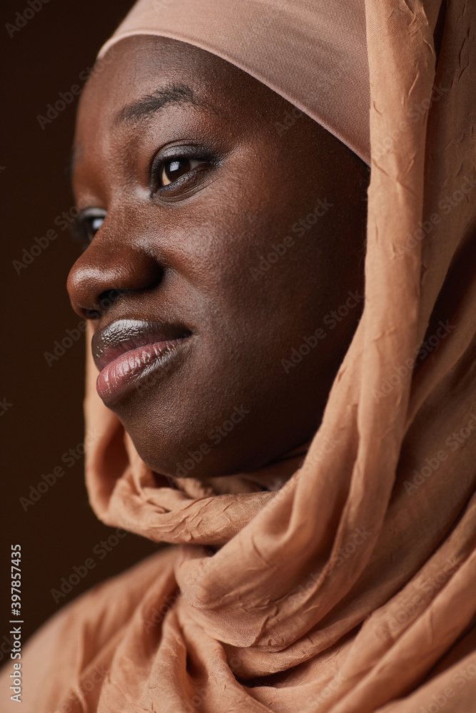 Vertical close up portrait of ethnic African-American woman wearing headscarf and looking away while posing in studio