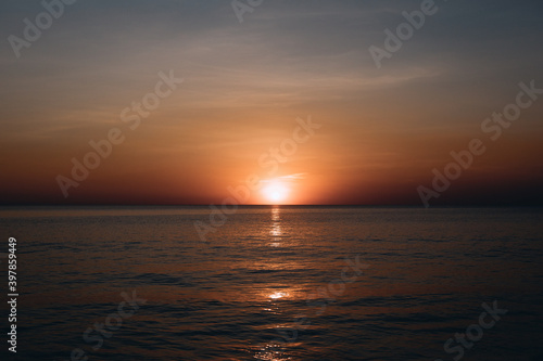 Breathtaking summer sunset view on the beach. Wonderful sunset landscape at the deep dark sea and orange sky above it and calm waves are flowing on it. © Semachkovsky 