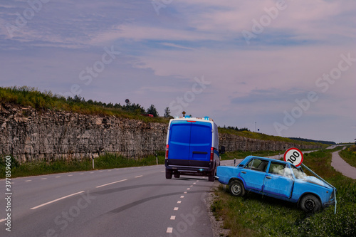 Police van stopped by a traffic accident scene where a A blue vintage car has lost control in a highway curve and crashed against a speed limit traffic sign