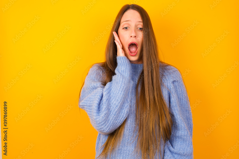 Shocked Young beautiful Caucasian woman wearing blue sweater against yellow wall looks with great surprisment being very stunned, astonished with unexpected news, Facial expressions concept. Shocked Young beautiful Caucasian woman wearing blue sweater against yellow wall looks with great surprisment being very stunned, astonished with unexpected news, Facial expressions concept.