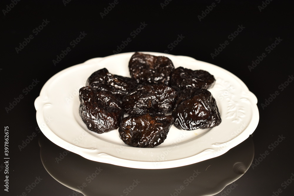 Sweet organic prunes on a white plate, close-up, on a black background. Sweet organic prunes on a white plate, close-up, on a black background.
