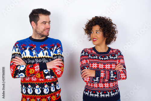 Dreamy rest relaxed Young couple wearing Christmas sweater standing against white wall crossing arms, looks good copyspace