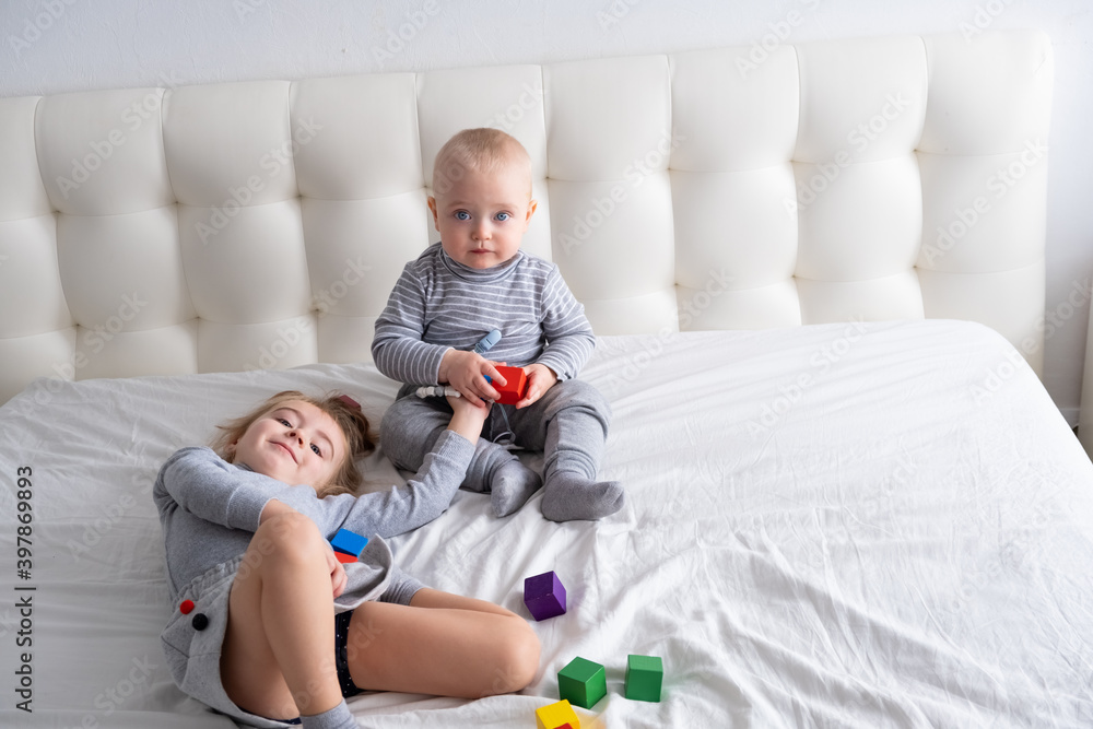 baby boy and little girl sister playing wooden toys at home on bed. Home activities for kids. baby boy and little girl sister playing wooden toys at home on bed. Home activities for kids.