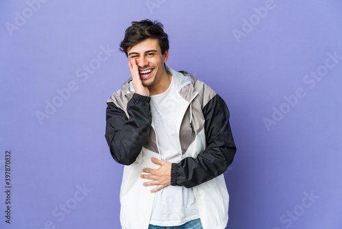 Young cool man laughs happily and has fun keeping hands on stomach.