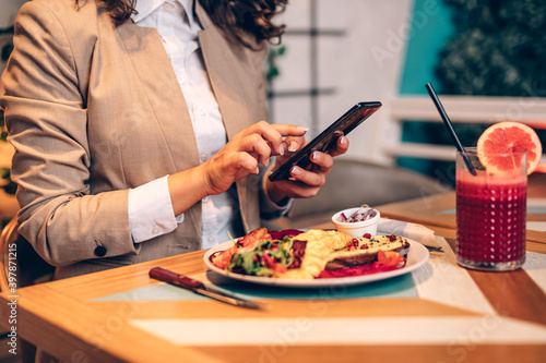 A middle-aged woman is sitting in a restaurant, typing a message on her mobile phone and enjoys a healthy meal and fresh beetroot and grapefruit juice.