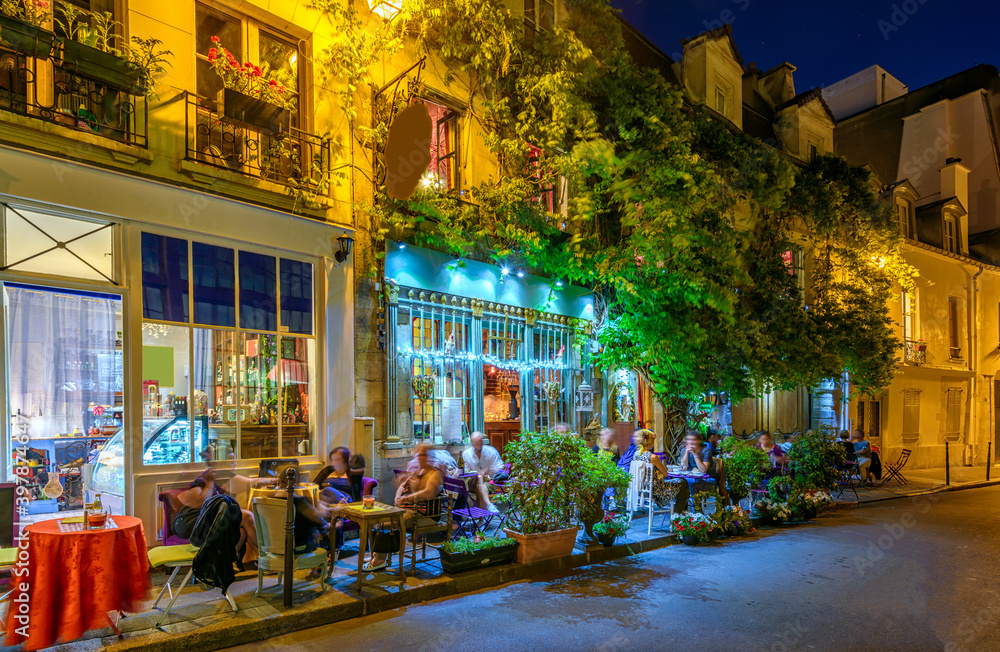 Night view of cozy street with tables of cafe in Paris, France