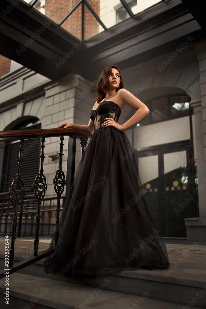 Fototapeta premium Full-length portrait of an elegant brunette woman with long hair in a black long evening dress.