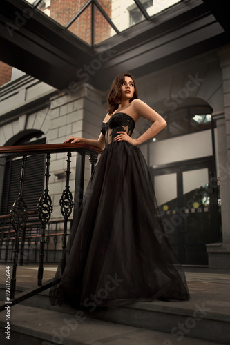 Full-length portrait of an elegant brunette woman with long hair in a black long evening dress.
