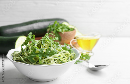 Delicious zucchini pasta with arugula in bowl on white wooden table
