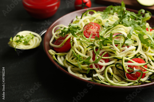 Delicious zucchini pasta with arugula and cherry tomatoes on black slate table, closeup