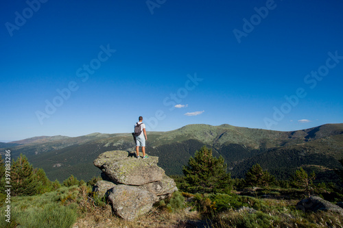 Man in sportswear on a big rock seeing the green valley on a sunny day on summer