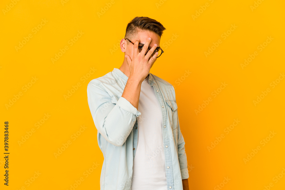 Young handsome caucasian man isolated blink at the camera through fingers, embarrassed covering face. Young handsome caucasian man isolated blink at the camera through fingers, embarrassed covering face.