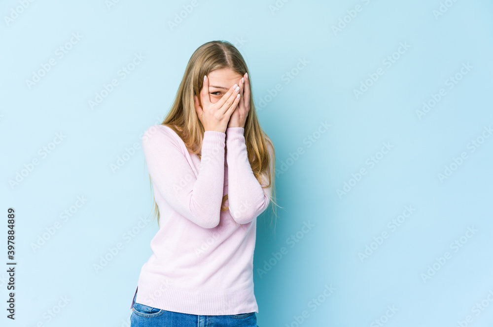 Young blonde woman isolated on blue background blink through fingers frightened and nervous. Young blonde woman isolated on blue background blink through fingers frightened and nervous.