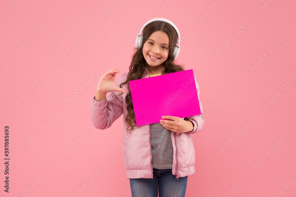 advertising technology. childhood development. girl presenting product. happy kid in headphones listen music. back to school. child hold empty paper for copy space. online education announcement advertising technology. childhood development. girl presenting product. happy kid in headphones listen music. back to school. child hold empty paper for copy space. online education announcement
