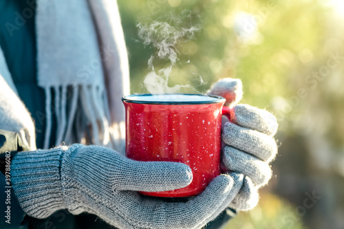 A cup of hot drink (tea, coffee or mulled wine) in winter nature. Female hand with a red cup. Winter relax comfort and mood.