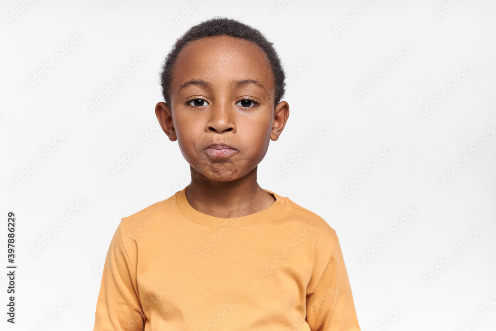 Isolated shot of displeased upset black little boy making unhappy grimace being disappointed because unfair grade at school or punishment. Sad dark skinned African child expressing disappointment Isolated shot of displeased upset black little boy making unhappy grimace being disappointed because unfair grade at school or punishment. Sad dark skinned African child expressing disappointment