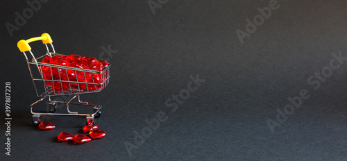 Shopping cart with glass red hearts-buying gifts for loved ones, couples in love on Valentine's day. Promotions in the holiday of lovers, products with love. Space for text, banner. Black background