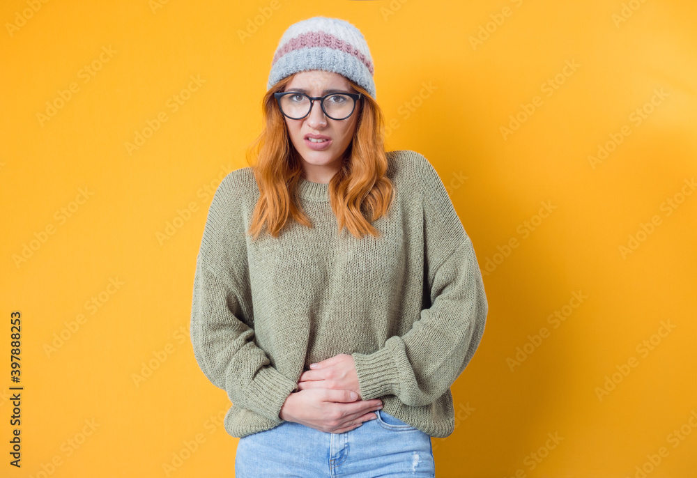 Young woman suffering from stomach pain. Pretty girl has food poisoning with hands on belly, isolated on yellow background Young woman suffering from stomach pain. Pretty girl has food poisoning with hands on belly, isolated on yellow background