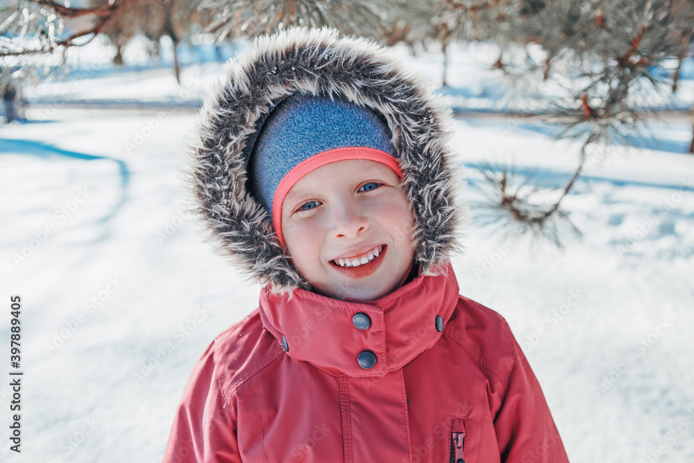 Cute adorable happy Caucasian smiling girl in pink jacket with fur hood during cold winter day. Kids outdoors seasonal activity. Funny face. Winter child portrait outside.
