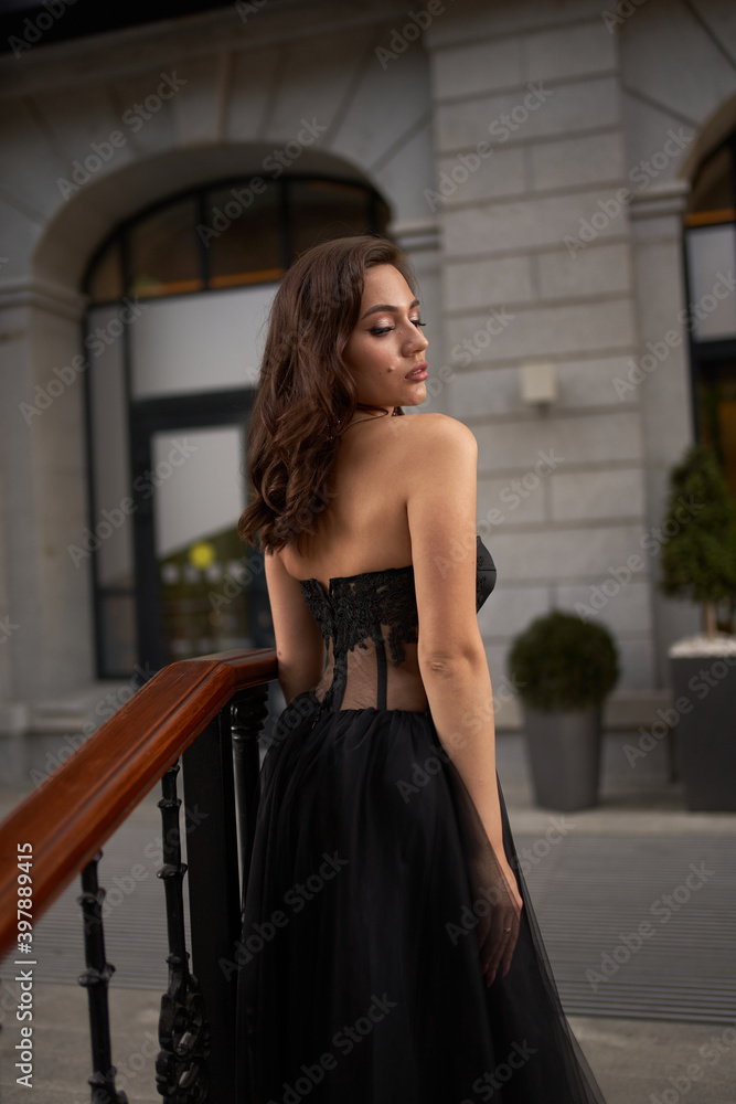 Full-length portrait of an elegant brunette woman with long hair in a black long evening dress.
