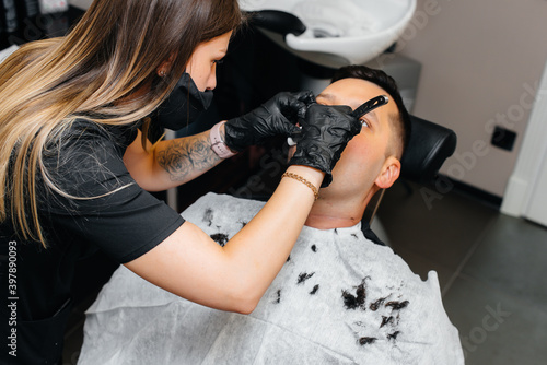 A professional stylist in a modern stylish barbershop shaves and cuts a young man's hair. Beauty salon, hair salon
