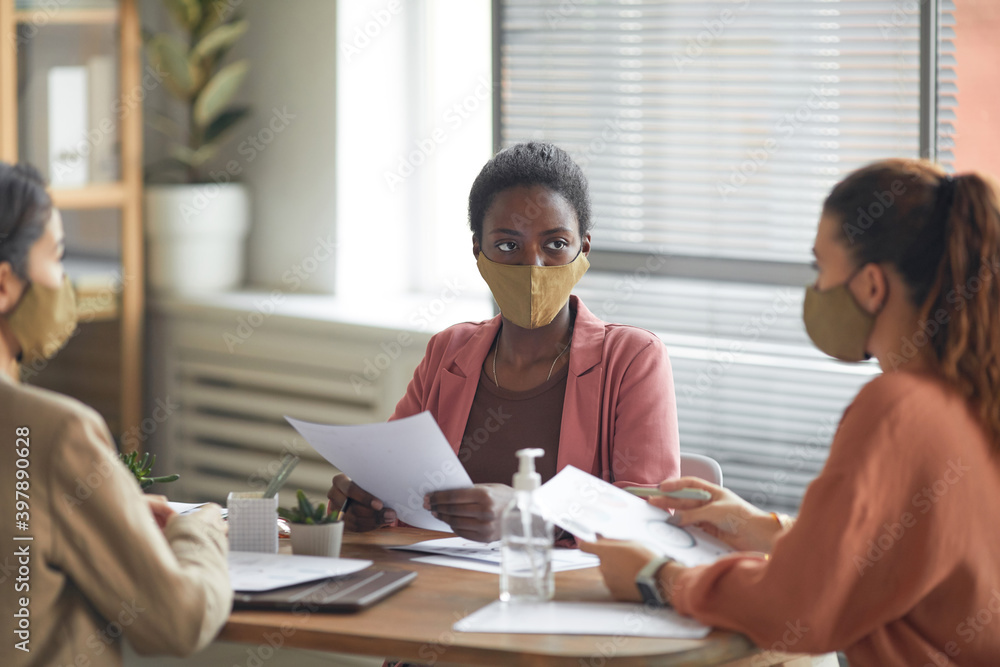 Portrait of young African-American businesswoman wearing mask while heading business meeting in office, copy space Portrait of young African-American businesswoman wearing mask while heading business meeting in office, copy space