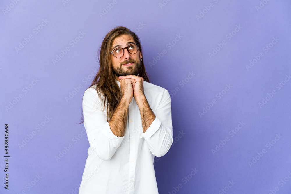 Young man with long hair look keeps hands under chin, is looking happily aside. Young man with long hair look keeps hands under chin, is looking happily aside.