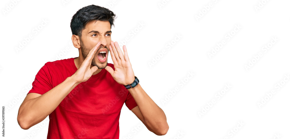 Young handsome man wearing casual red tshirt shouting angry out loud with hands over mouth Young handsome man wearing casual red tshirt shouting angry out loud with hands over mouth