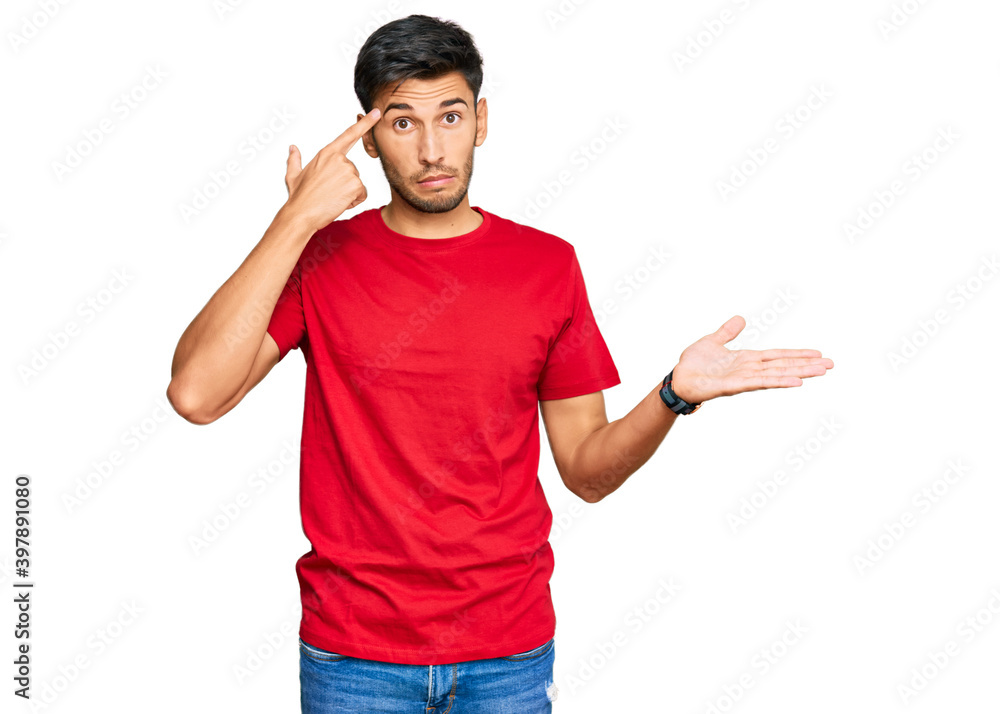 Young handsome man wearing casual red tshirt confused and annoyed with open palm showing copy space and pointing finger to forehead. think about it. Young handsome man wearing casual red tshirt confused and annoyed with open palm showing copy space and pointing finger to forehead. think about it.