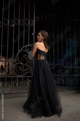 Full-length portrait of an elegant brunette woman with long hair in a black long evening dress.