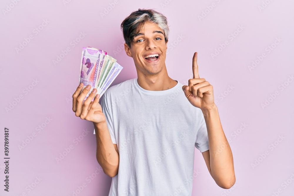 Young hispanic man holding indian rupee banknotes smiling with an idea or question pointing finger with happy face, number one Young hispanic man holding indian rupee banknotes smiling with an idea or question pointing finger with happy face, number one