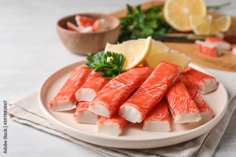 Plate of fresh crab sticks with lemon on white table, closeup