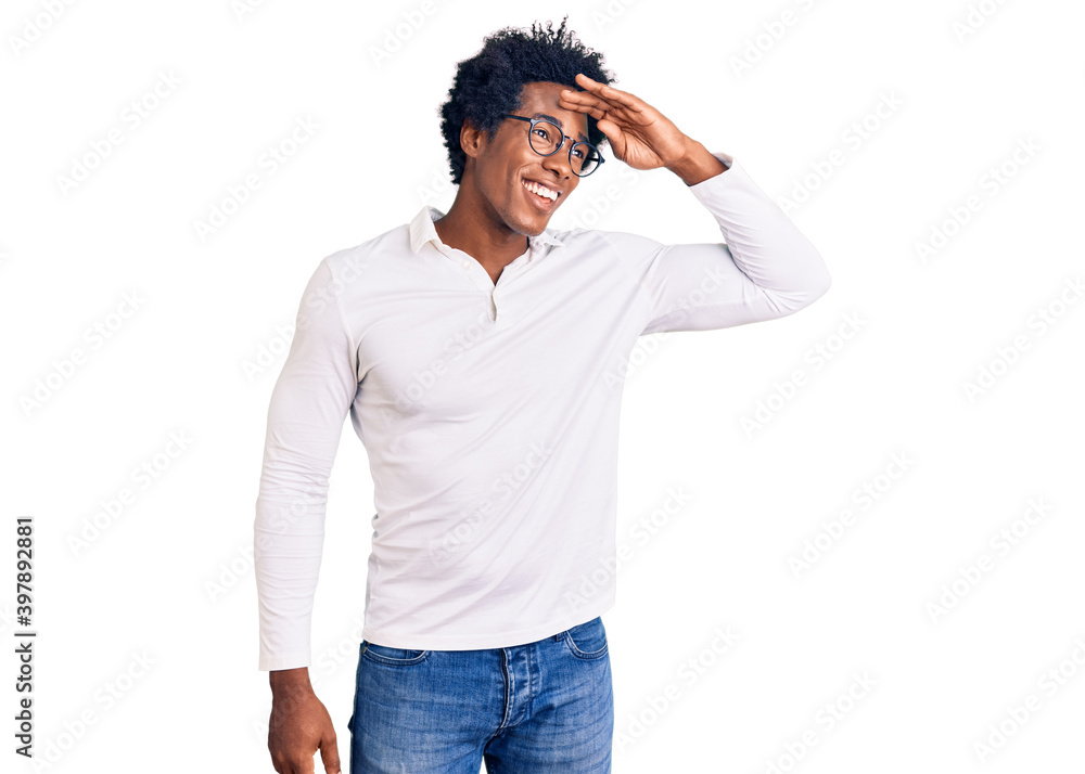 Handsome african american man with afro hair wearing casual clothes and glasses very happy and smiling looking far away with hand over head. searching concept. Handsome african american man with afro hair wearing casual clothes and glasses very happy and smiling looking far away with hand over head. searching concept.