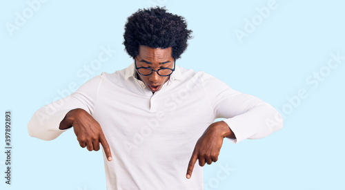 Handsome african american man with afro hair wearing casual clothes and glasses pointing down with fingers showing advertisement, surprised face and open mouth