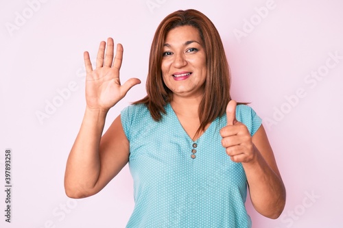 Middle age brunette hispanic woman wearing casual clothes showing and pointing up with fingers number six while smiling confident and happy.