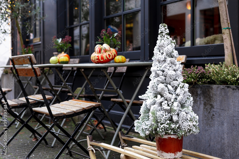 Christmas tree in snow in street cafe. New Year and Christmas in European vintage retro style near outdoor tables with chairs on cafe terrace. Christmas Fair street food