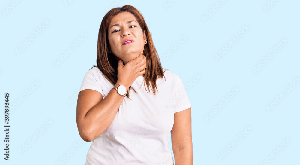 Middle age latin woman wearing casual white tshirt touching painful neck, sore throat for flu, clod and infection Middle age latin woman wearing casual white tshirt touching painful neck, sore throat for flu, clod and infection