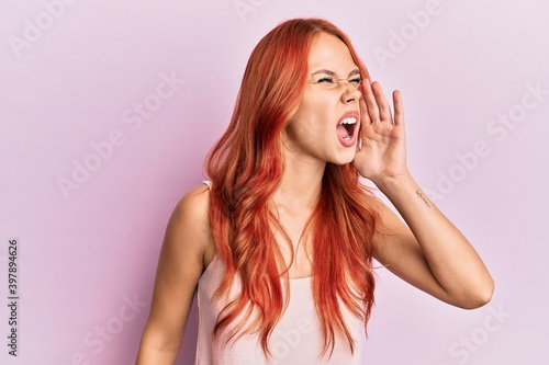 Young beautiful redhead woman wearing casual clothes over pink background shouting and screaming loud to side with hand on mouth. communication concept.