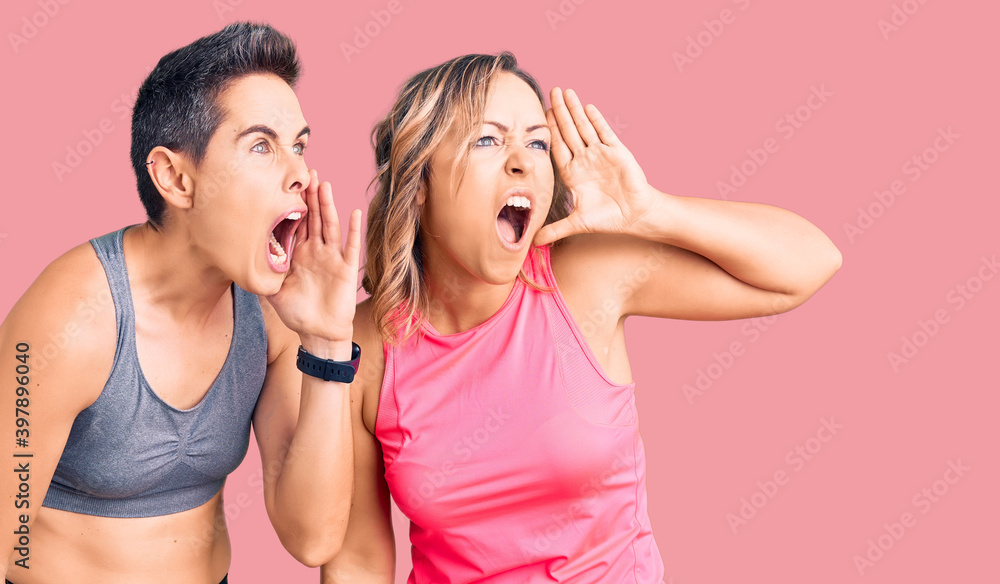 Couple of women wearing sportswear shouting and screaming loud to side with hand on mouth. communication concept. Couple of women wearing sportswear shouting and screaming loud to side with hand on mouth. communication concept.