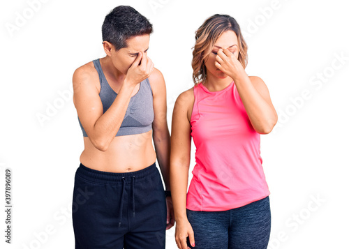 Couple of women wearing sportswear tired rubbing nose and eyes feeling fatigue and headache. stress and frustration concept.