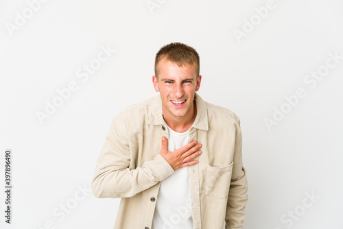 Young caucasian handsome man laughs out loudly keeping hand on chest.